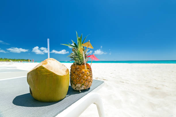 Sweet pineapple and coconut cocktail on sand with caribbean beach background. Travel summer vacation banner with copy space for your text