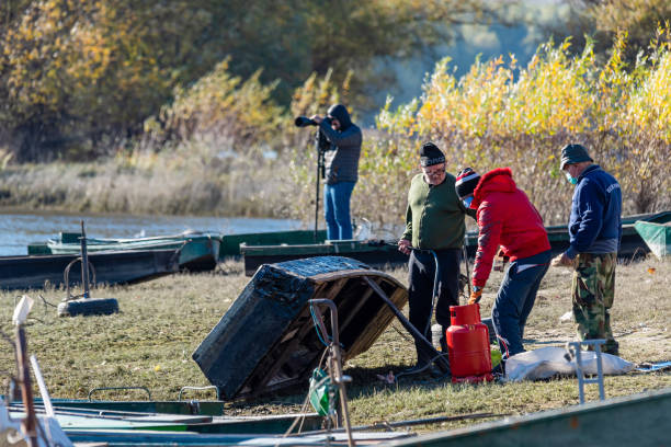 아침에 다뉴브 강에서 보트를 수리하는 남자들. 어부들이 배를 정리하고 수리하고 있습니다. - boathouse work tool equipment old 뉴스 사진 이미지