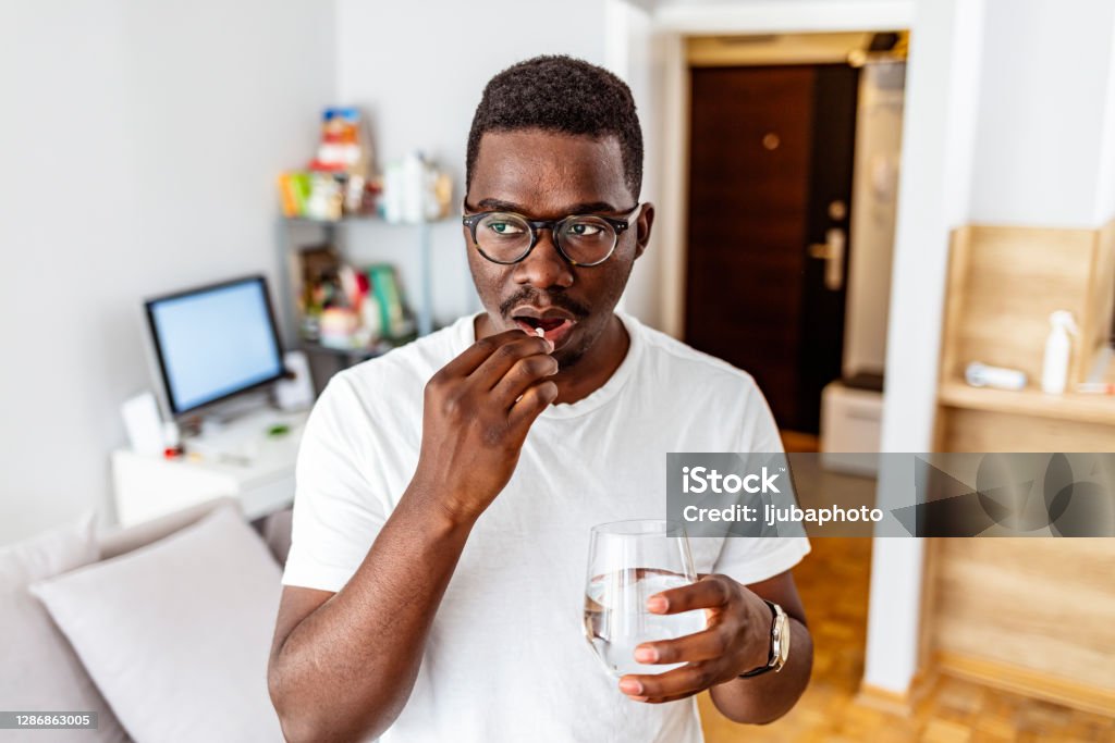 Managing pain so he can get back to being productive Shot of a young man taking medication while standing at home during the day. Men Stock Photo