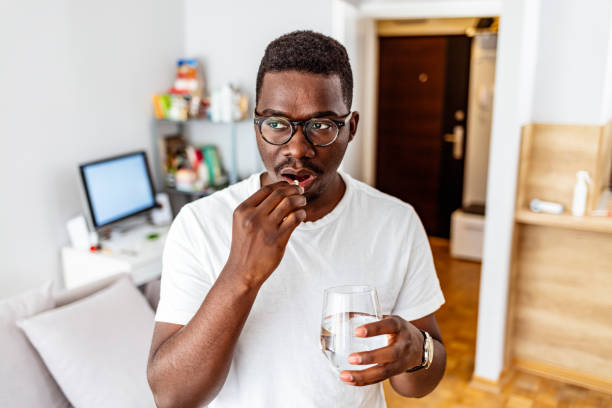 Managing pain so he can get back to being productive Shot of a young man taking medication while standing at home during the day. aspirin photos stock pictures, royalty-free photos & images