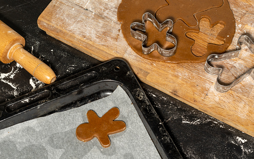 Unbaked gingerbread man cookie on oven tray with rolled cookie dough, cookie cutters and rolling pin.