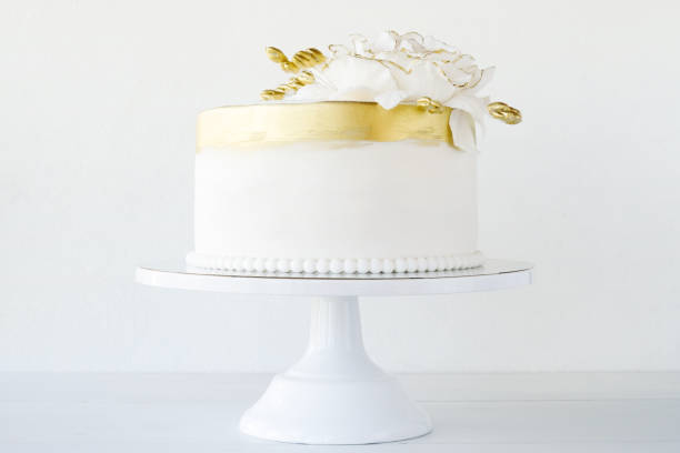 istock White wedding cake decorated with gold flowers on a white background. 1286877280