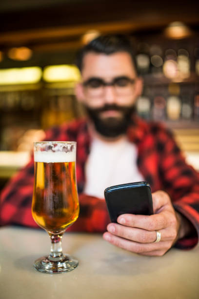 homem desfocado olhando telefone, foco é na cerveja, foco é no telefone - beer glass mustache beer color image - fotografias e filmes do acervo