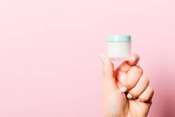 istock Female hand holding cosmetics jar at pink background with empty space for your design 1286883095