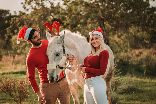 Young happy christmas couple with their white horse in nature in Majorca