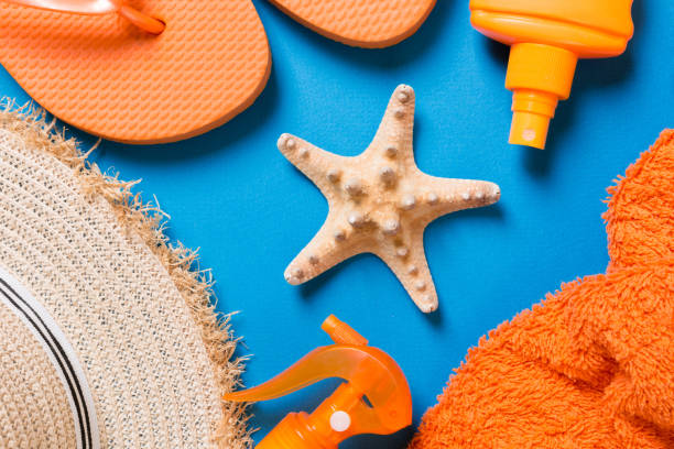 istock Summer beach flat lay accessories. Sunscreen bottle cream, straw hat, flip flops, towel and seashells on colored Background. Travel holiday concept with copy space 1286883655