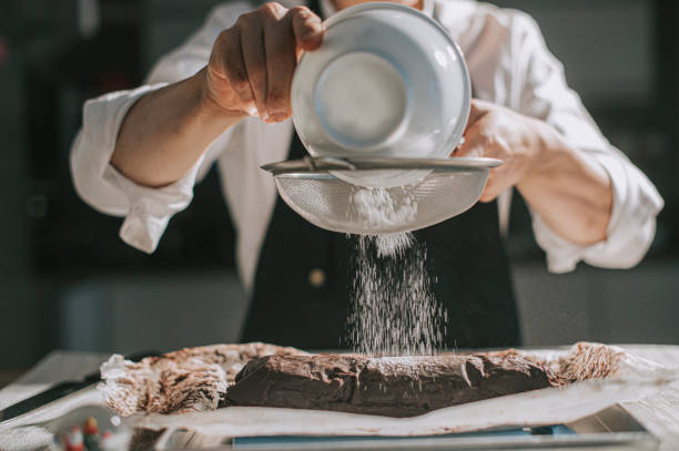asian chinese dessert chef dusting on chocholate sweet food shortbread in kitchen asian chinese dessert chef dusting on chocholate sweet food shortbread in kitchen sprinkling powdered sugar stock pictures, royalty-free photos & images