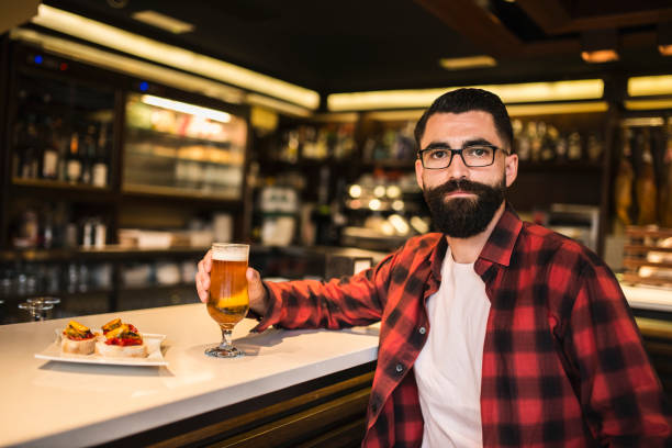 istock Hipster in Bar drinking alcohol. Beer and tapas. Posing serious with ambient light. 1286888469
