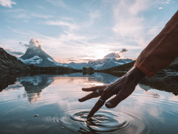 Female's finger touching water surface from alpine lake below the Matterhorn peak