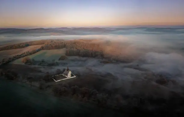 Photo of Aerial view of the Chapel near Moravian royal castle Veveri (Burg Eichhorn), standing on a rock above water dam on the river Svratka, early morning light and autumn weather with the green forest.