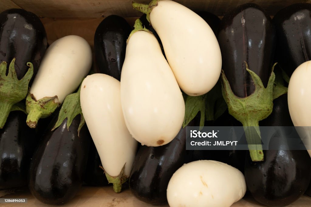 White and black eggplants on a market stall eggplants in a pile in a wooden crate. Aubergine Blanche is an old variety. White Eggplant Stock Photo