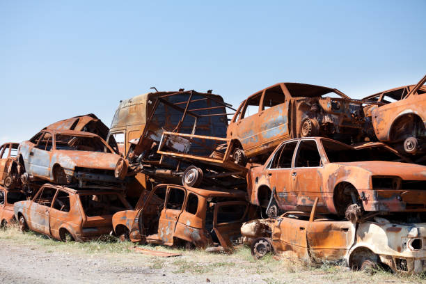Stack of damaged rusted car scraps on junkyard. Different models and types of car. Clear blue sky in background