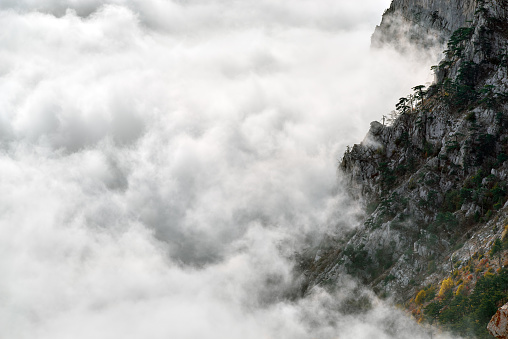 View of the slope rocky mountain above fog and clouds. Creamy