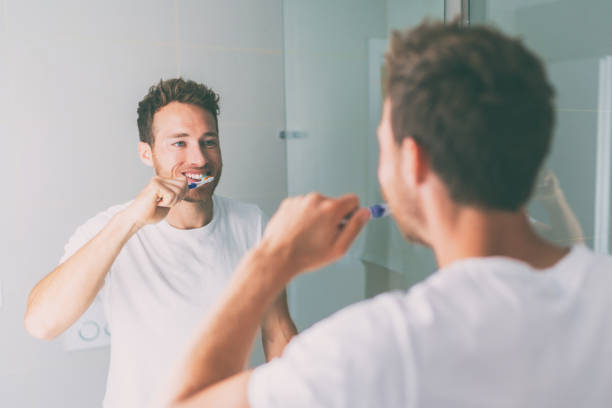 istock Brushing teeth man looking in mirror of home bathroom using toothbrush in morning routine for clean dental oral care 1286911542