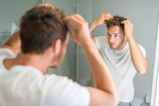 Pérdida de cabello hombre mirando en el espejo del baño poner cera tocando su peinado o comprobar si hay problemas de pérdida de cabello. Problema masculino de pérdida de cabellos photo