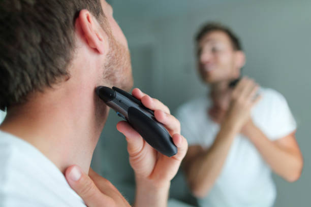 hombre afeitado barba usando afeitadora eléctrica. concepto de peluquería de belleza masculina. hogar estilo de vida joven persona mirando el espejo del baño recortando el pelo en el cuello - wet shave fotografías e imágenes de stock