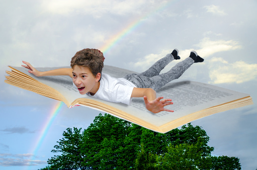 Boy flying on a book  seen from side,\nThis is to represent the pleasure of reading and the fact that reading is making the reader traveling to many worlds, magical or real.