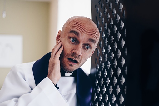 Surprised young vicar priest in the confession booth