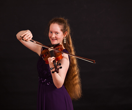 15 year old girl in a home studio setting against a dark background, playing the violin. Copy space provided.