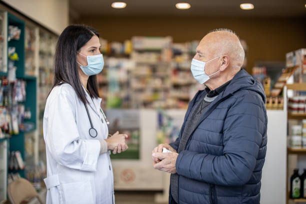 istock Female pharmacist wearing face mask while standing and talking with elderly male customer in pharmacy 1286928160