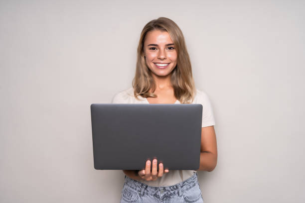 istock Young smiling confident woman using laptop and looking camera isolated over white 1286928232