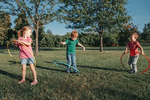 Cute smiling Caucasian preschool girl boys friends playing with hoola hoop in park outside. Kids sport activity. Lifestyle happy childhood. Summer seasonal outdoor game fun for kids children.