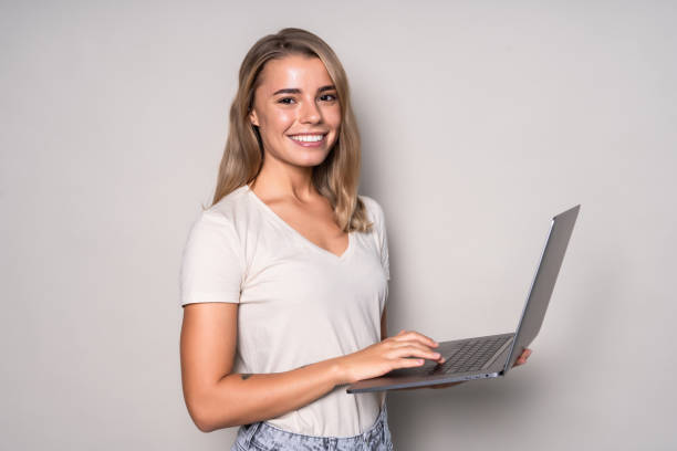 istock Young smiling confident woman using laptop and looking camera isolated over white 1286930042