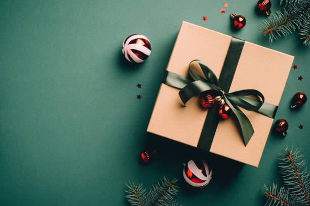 istock Cardboard gift box with ribbon bow, for tree branches and red balls on green table. Vintage Christmas background. Retro style New year present. Flat lay, top view, copy space. 1286938633