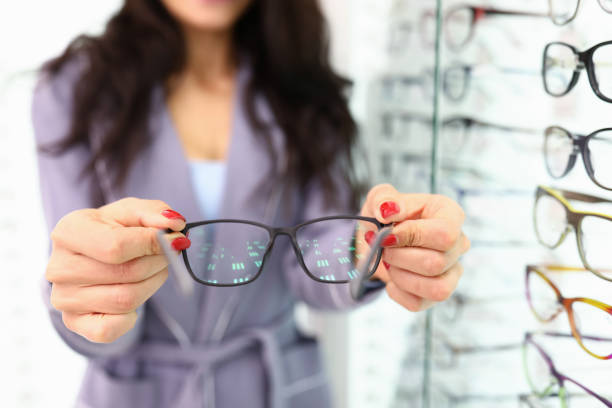 istock Female hands hold black-framed glasses next to an optics showcase 1286940829