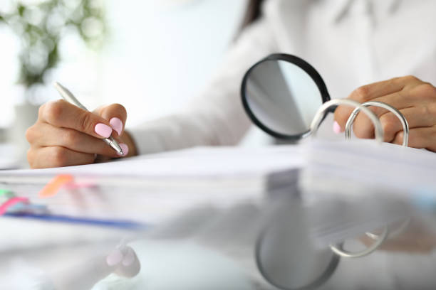 istock Female hands hold magnifying glass and pens next to documents. 1286940830