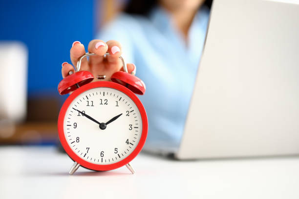 istock Woman's hand lies on red alarm clock next to laptop. 1286940845