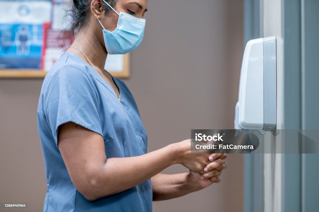 Nurse sanitizes hands A nurse uses a hand sanitizing dispenser in the clinic. Hand Sanitizer Stock Photo