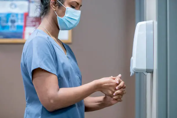 A nurse uses a hand sanitizing dispenser in the clinic.