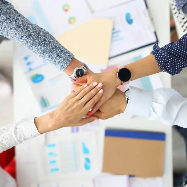 Photo of Business employees folded their hands together over work table.