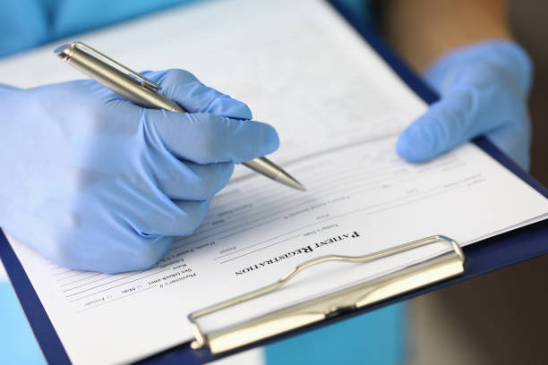 Gloved hand holds clipboard and pen and fills out patient registration form Gloved hand holds clipboard and pen and fills out patient registration form. Reception of patients in medical institutions concept restraining device stock pictures, royalty-free photos & images