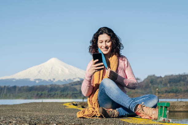 A young woman removes her face mask to take a selfie with her mobile phone. A young woman removes her face mask to take a selfie with her mobile phone during a holiday after quarantine. Beautiful background Snowy Villarrica Volcano, Chile chile tourist stock pictures, royalty-free photos & images