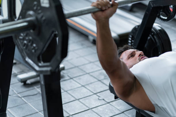 istock Athlete performs his weightlifting with the bar and the discs while lying on the flat-chest bench in sportswear 1286948450