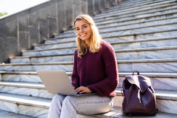 istock Smiling young woman sitting outdoors with laptop computer and coffee cup 1286958315