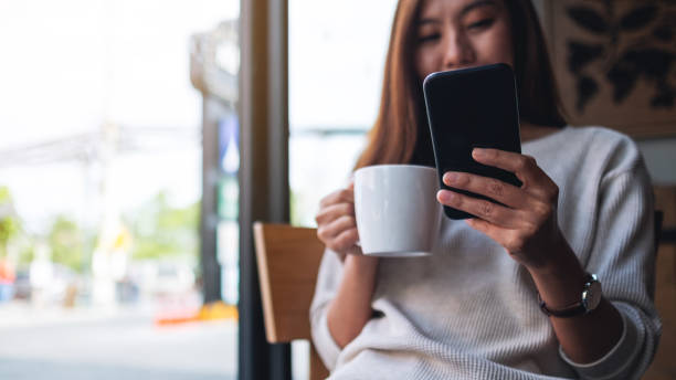 istock a beautiful asian woman holding and using mobile phone while drinking coffee in cafe 1286966912