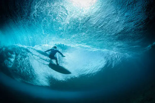 A surfer falls back onto a wave, viewed from beneath the wave showing the texture of the crystal clear water