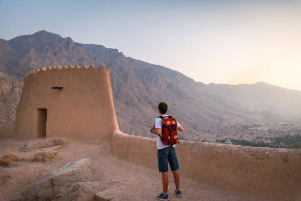 Man visiting Dhayah Fort in north Ras Al Khaima in the UAE Man visiting middle eastern Dhayah Fort in north Ras Al Khaimah, United Arab Emirates on the desert mountain top at sunset. Caucasian man traveling to Middle East jebel hafeet stock pictures, royalty-free photos & images