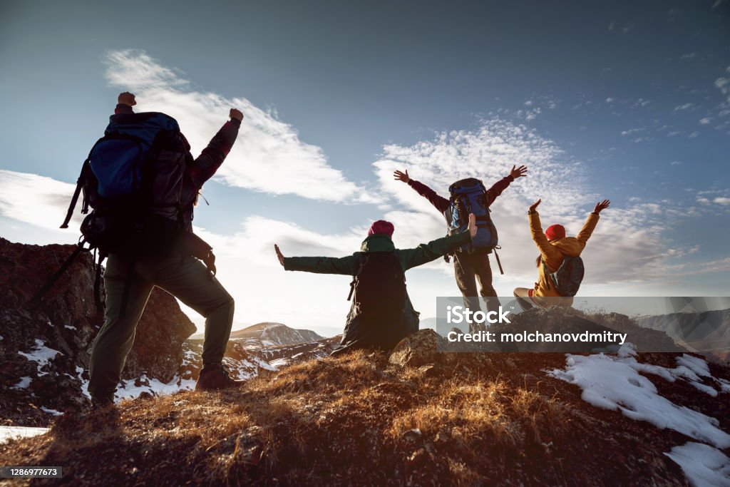 Hikers in winner poses stands at mountain top Four happy hikers stands in winner poses at mountain top at sunset time Hiking Stock Photo