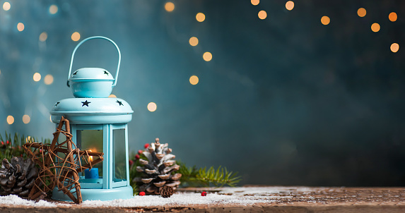 Candle in a holder with Christmas and New Year winter holidays symbols on a illuminated festive table with blue festive copy space background