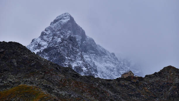 vista mozzafiato sul rifugio hintergrathütte situato sulla cresta nella parte orientale dei monti ortler aspre e innevati che sono in parte coperti da nuvole in alto adige, alpi, italia. - sulden foto e immagini stock