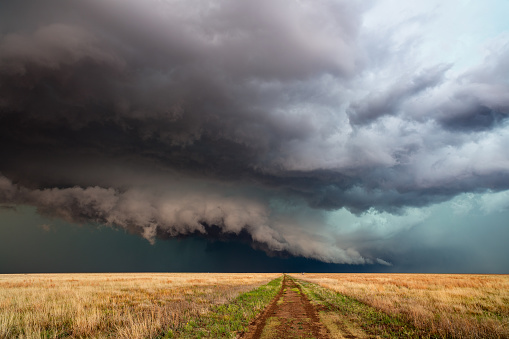 Dramatic clouds and stormy sky with a thunderstorm over a dirt road and field in Kansas.