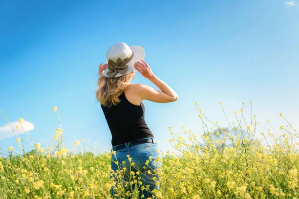 Blonde girl in white hat posing in a rapeseed field