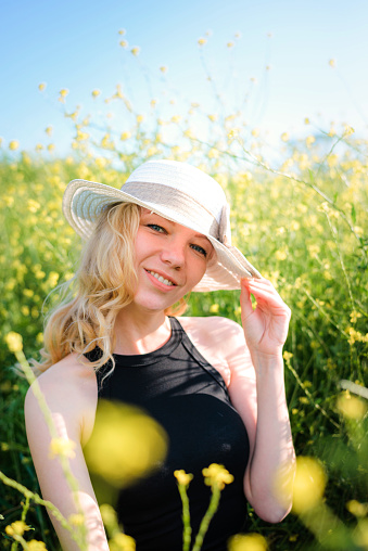 Blonde girl in a black bodysuit and white hat posing in a rapeseed field