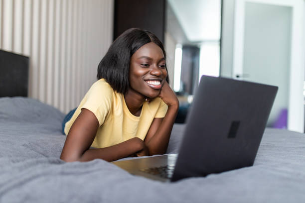 istock Smiling african woman using laptop on bed 1286990759