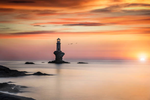 Romantic sunrise behind the famous Tourlitis lighthouse Romantic sunrise behind the famous Tourlitis lighthouse situated on a steep rock in the sea at the cycladic island of  Andros, Greece andros island stock pictures, royalty-free photos & images