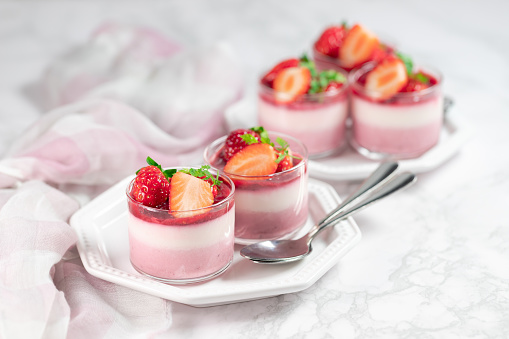 Traditional italian dessert vanilla strawberry panna cotta in a glass with fresh berries on a marble background.